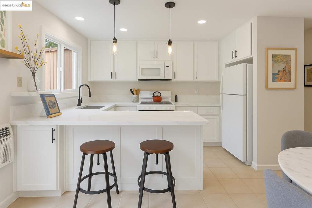 Kitchen featuring a peninsula, white appliances, a kitchen bar, recessed lighting, and white cabinetry at 3055 Treat Blvd #25, Concord, CA 94518